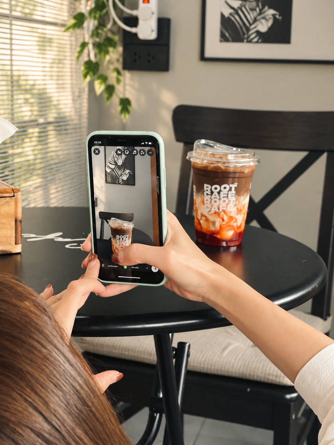 A guest photographs an iced coffee in Root Cafe's branded cup.