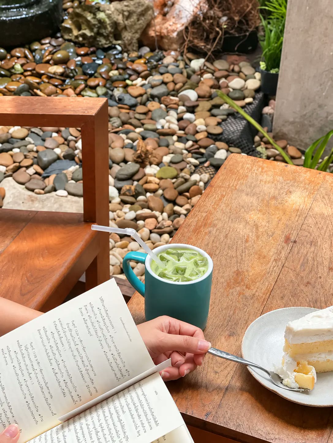 Iced matcha, coconut cake and a book beside the pebble garden.